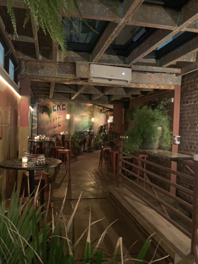 Candlelit courtyard patio with plants, bistro tables, and a mural