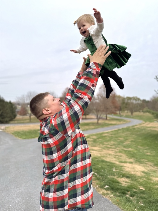 Dad lifting his toddler daughter into the air in a park