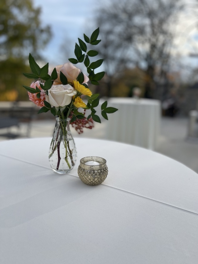 Bud vase of roses and greenery beside a votive on a cocktail table